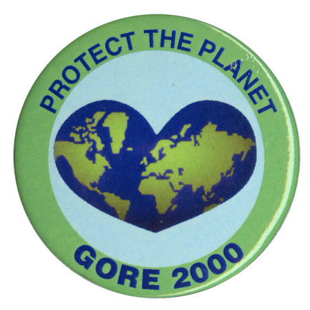 Round button with green border and a white center that includes a blue and green heart-shaped image of the Earth. Blue text reads "PROTECT THE PLANET GORE 2000"