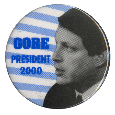 Round button with a black and white photograph of Al Gore against a background of blue and white stripes. Blue text reads "GORE PRESIDENT 2000"