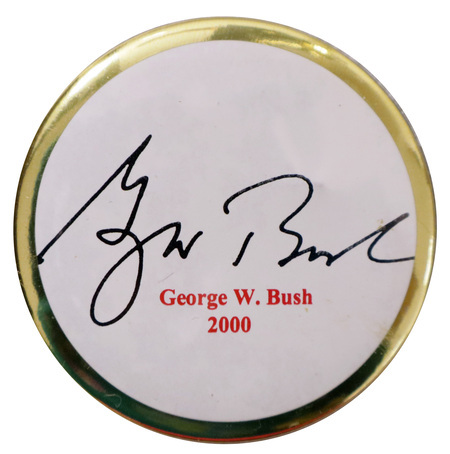Round, white button with a gold border containing George W. Bush's signature in black and red text reading "George W. Bush 2000"