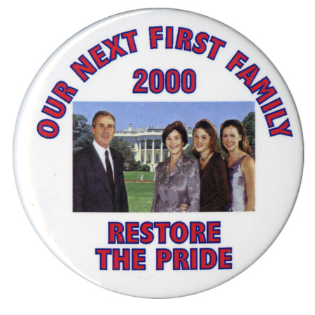 Round, white button with a color photograph of George W. Bush, Laura Bush, Barbara Bush, and Jenna Bush against a color photograph of the White House. Red text reads "OUR NEXT FIRST FAMILY 2000 RESTORE THE PRIDE"