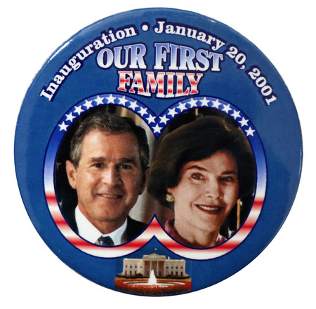 Round, blue button with color photographs of George W. and Laura Bush in a frame with the red, white, and blue stars and stripes of the US flag. Below their photographs is a color photograph of the White House. White, red, and blue text reads "Inauguration January 20, 2001 OUR FIRST FAMILY"