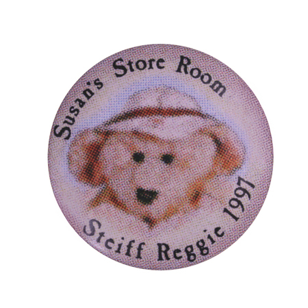 Round button with a color image of a teddy bear wearing a hat. Black text reads "Susan's Store Room Steiff Reggie 1997"