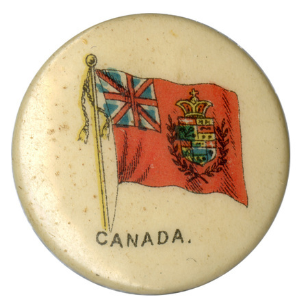 Round, white button with a color illustration of the Canadian Red Ensign Flag, red with a Union Jack in the top left corner and an elaborate shield in the center. Black text reads "CANADA."