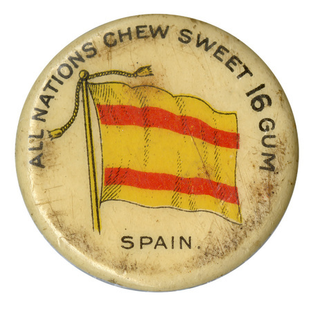 Round, white button with a color illustration of the historical merchant marine flag of Spain, horizontal red stripes on a yellow field. Black text at the bottom reads "SPAIN."