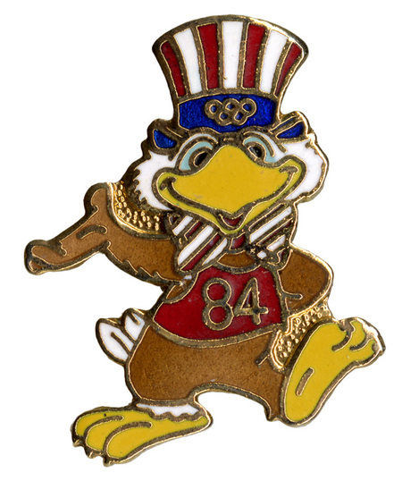 Enameled button in the shape of Sam the Olympic Eagle, a bald eagle wearing a red, white, and blue top hat and bowtie, as well as a red jersey with the number "84".