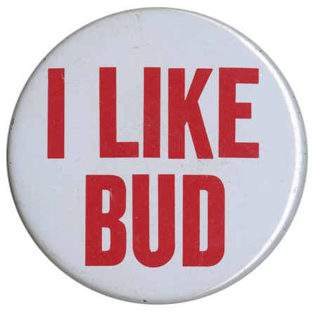 Round, white button with red text reading "I LIKE BUD"