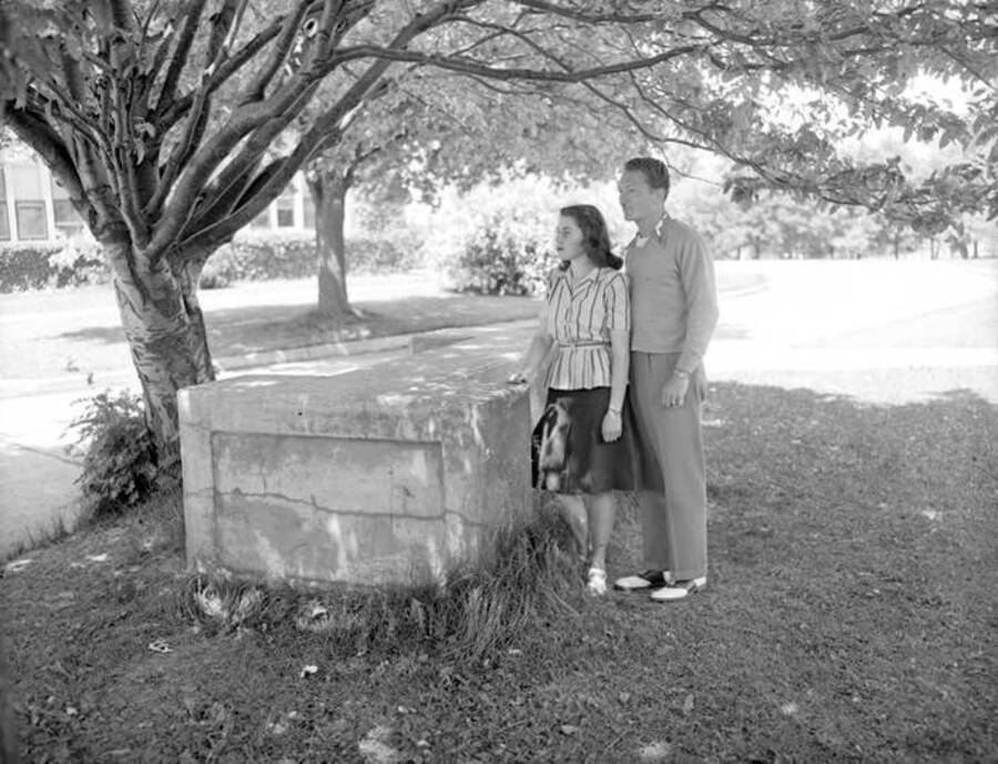 1961 photograph of the I Bench. Two students pose next to the bench, Administration Building in background. [PG1_101-04]