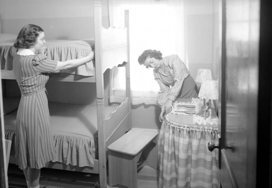 1945 photograph of the Home Management House. Two female students set up a bedroom. [PG1_106-11]