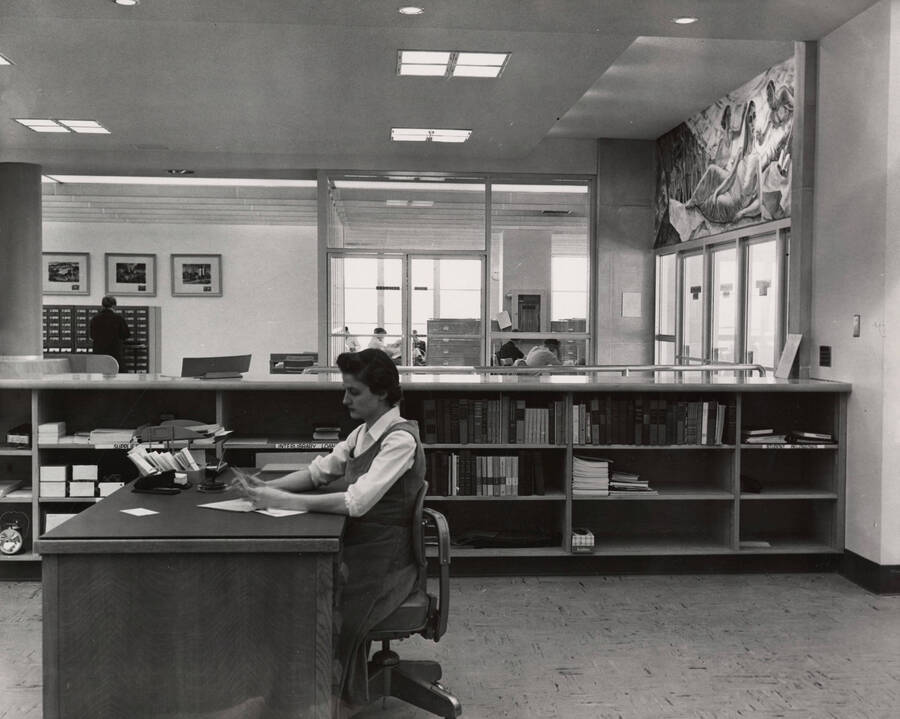 1957 photograph of the Library. Woman at loan desk in foreground. [PG1_122-015]