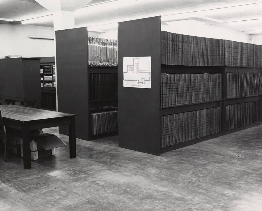1957 photograph of the Library. Newspaper storage area with table to left. [PG1_122-036]