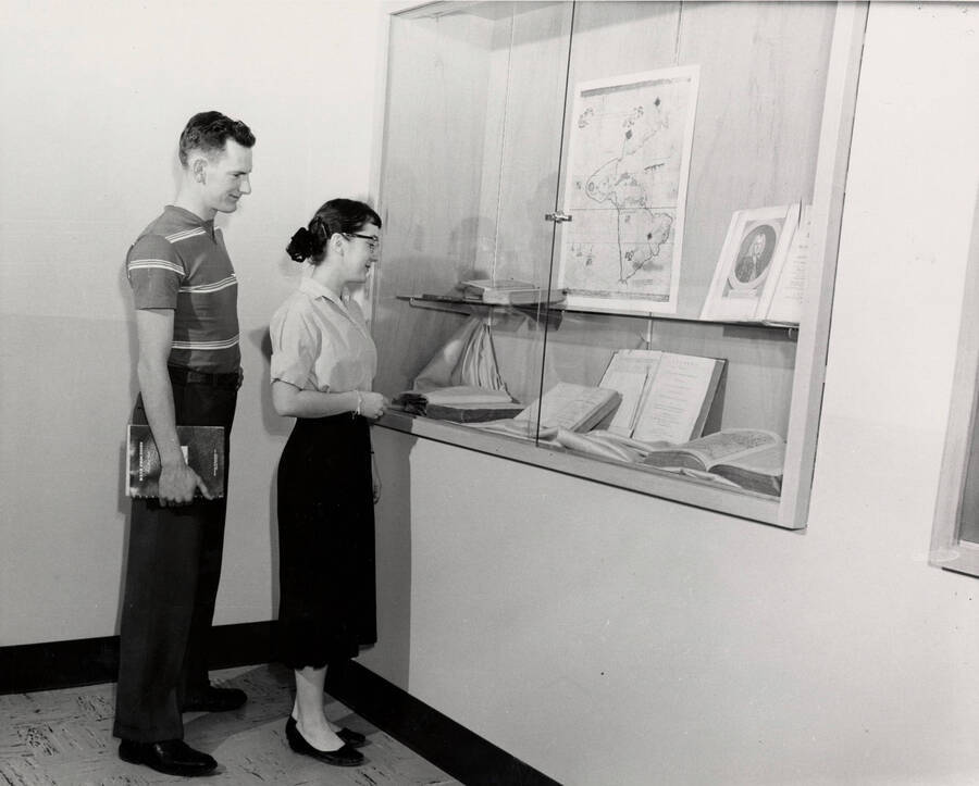 1957 photograph of Library. Two students examine the contents of a display case. [PG1_122-040]