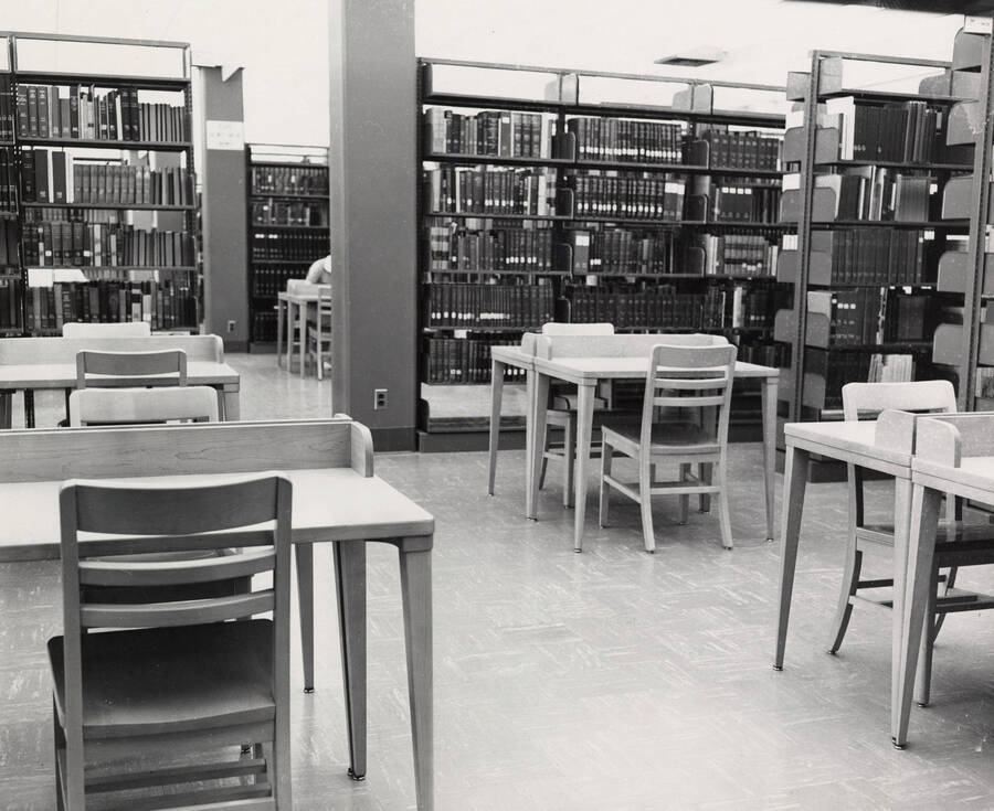 1957 photograph of the Library. Study area with four tables in foreground, student at work in background. [PG1_122-045]