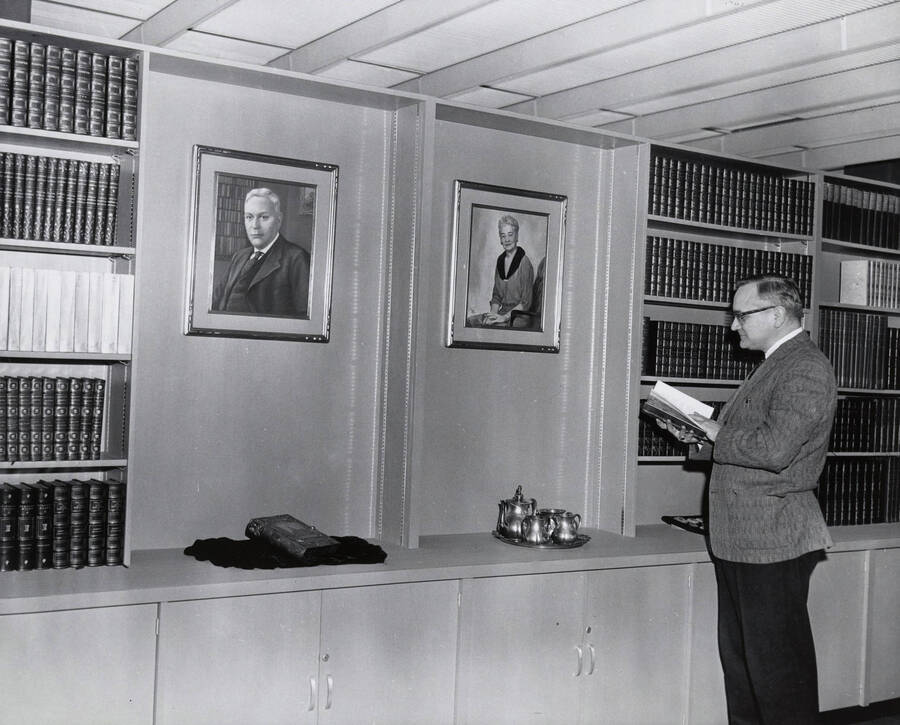 1962 photograph of the Library. Charles Webbert reads a book next to two portraits. [PG1_122-065]