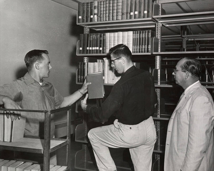 1957 photograph of the Library. Moving books into the new library, left to right: Lee Shellman, Mike McQuade, Edmond Gnoza. Donor: Publications Dept. [PG1_122-069]