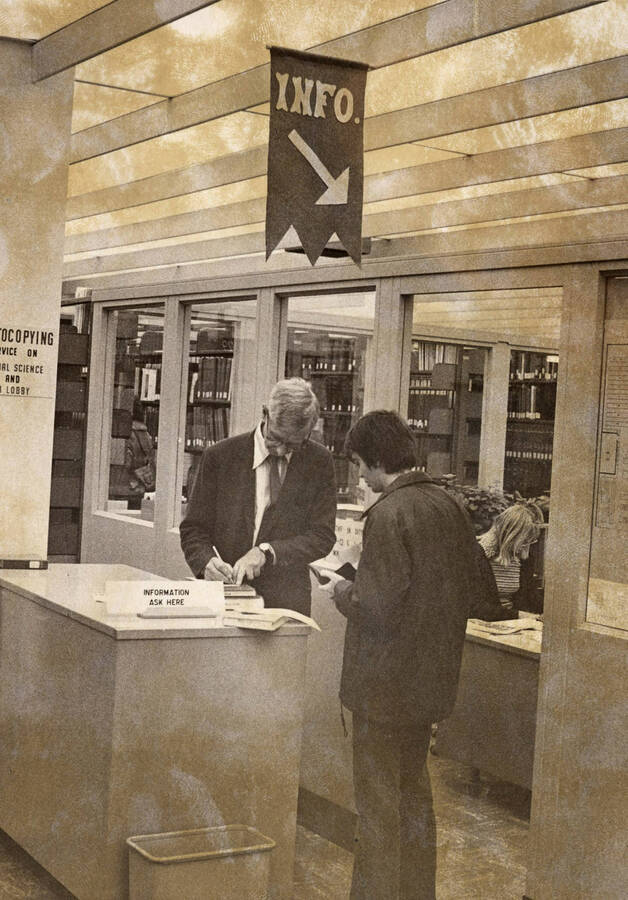1977 photograph of the Library. Rod Hardies helps a student. [PG1_122-084]