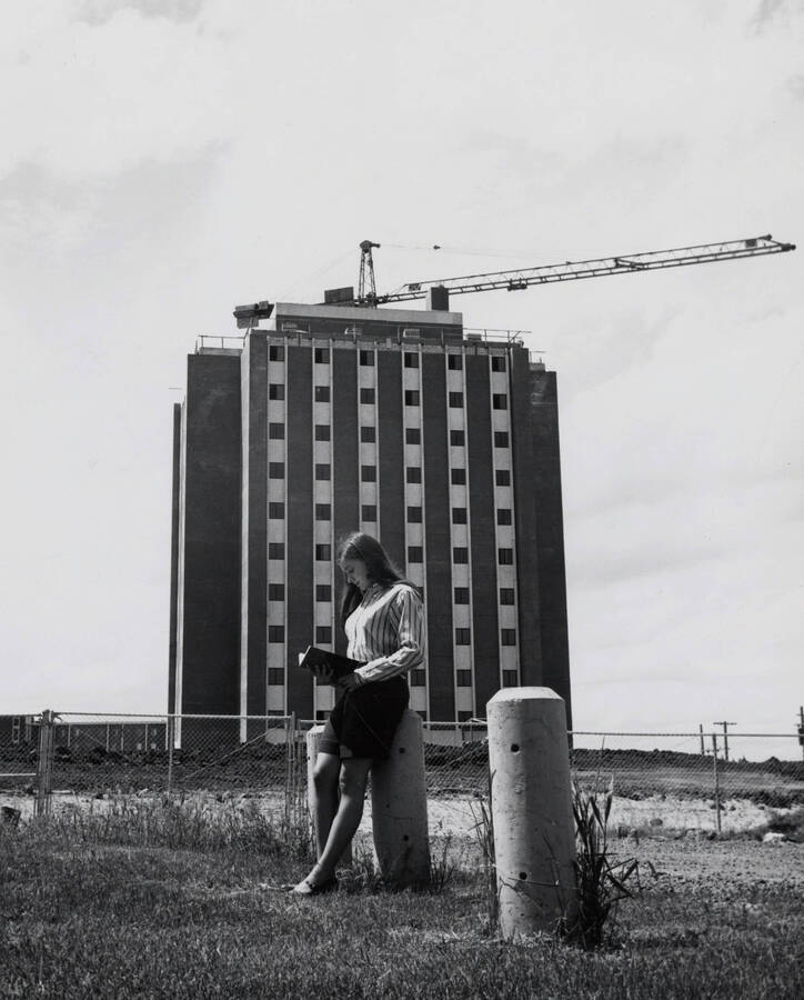 1969 photograph of the Donald R Theophilus Residence Hall under construction. A student reads a book in foreground. Donor: Publications Dept. [PG1_134-02]