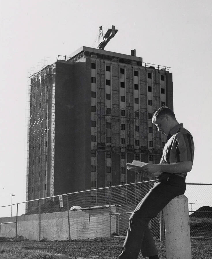 1969 photograph of the Donald R Theophilus Residence Hall under construction. A student reads a book in foreground. Donor: Photo Center. [PG1_134-09]