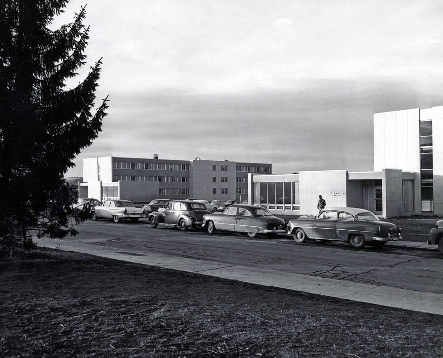 1957 photograph of the William J. McConnell Residence Hall. Automobiles and student in foreground. Donor: Publications Dept. [PG1_142-05]