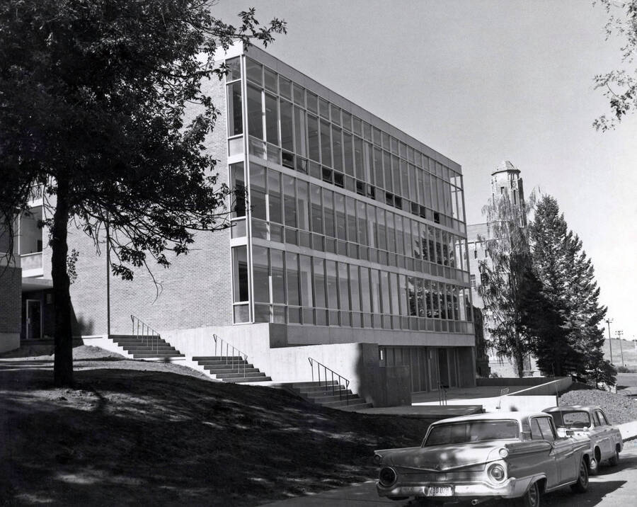 1966 photograph of the Art and Architecture Building. Automobiles in foreground, Memorial Gym in background. [PG1_143-01]
