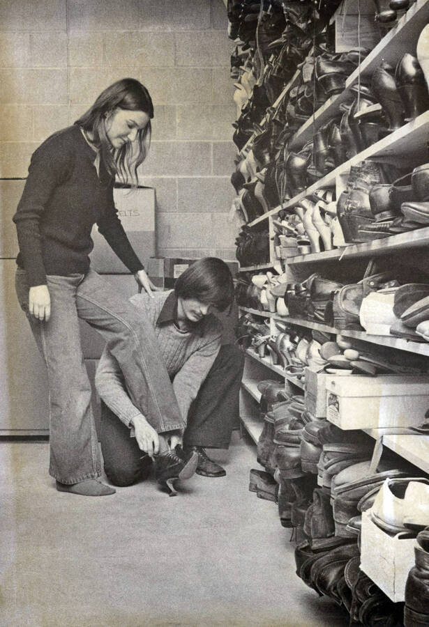 1975 photograph of Hartung Theatre. Students try on shoes in the costume storage area. [PG1_145-13]