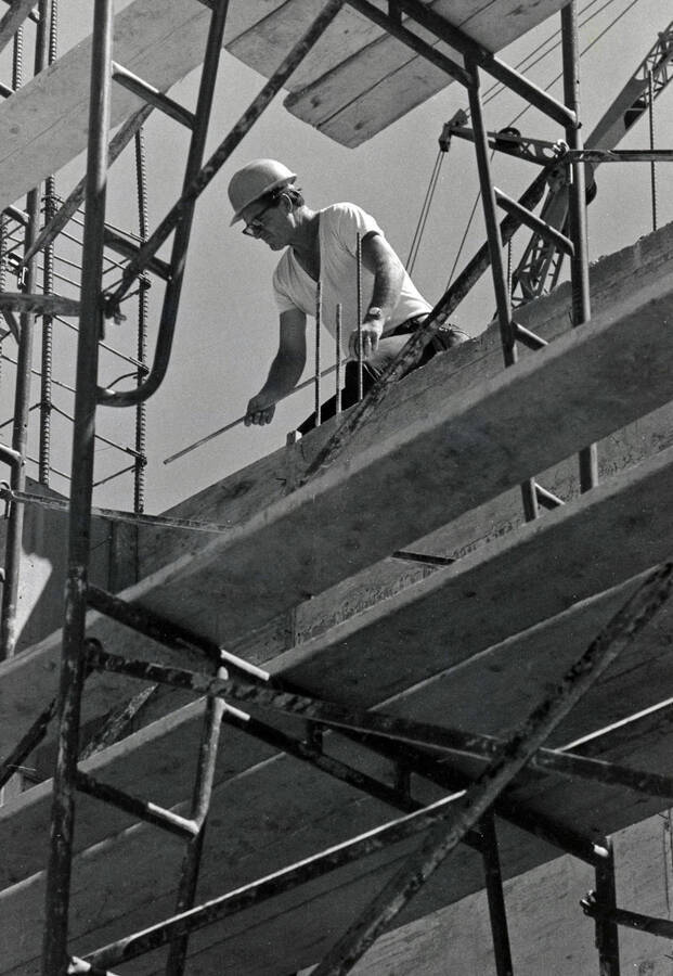 1974 photograph of the Menard Law Building under construction. Construction worker in foreground on scaffolding. [PG1_162-11]