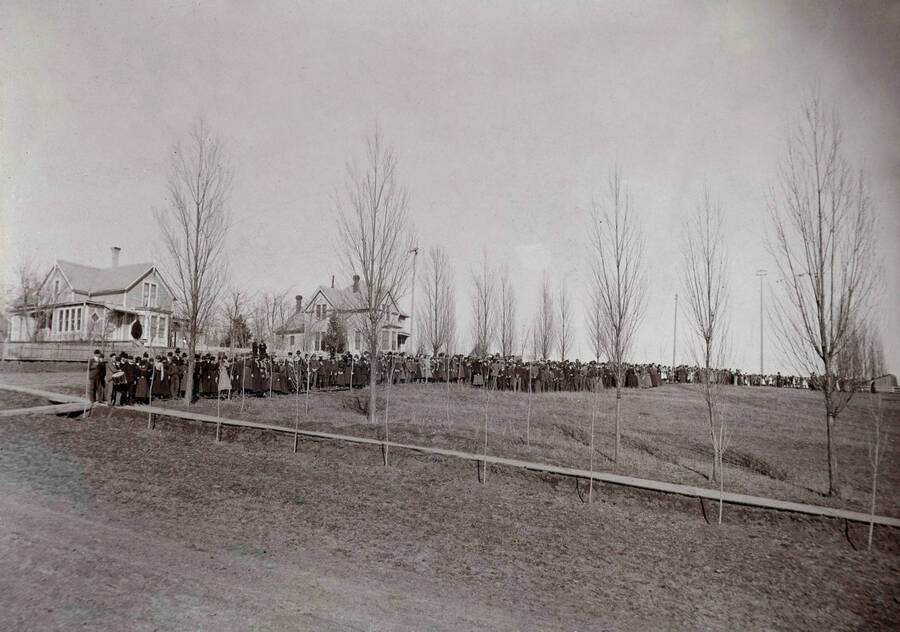 1897 panoramic photograph of University of Idaho campus. Students lined up for procession on sidewalk. Donor: Homer David. [PG1_002-29]