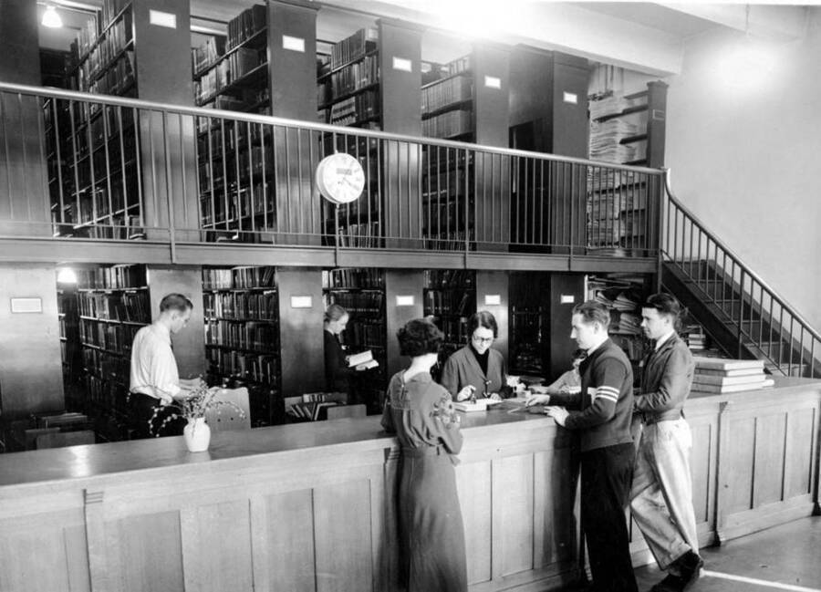 1936 photograph of the Library. Students receive help from librarians at the loan desk. [PG1_201-10]