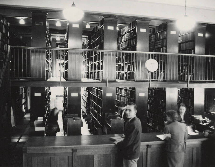 1937 photograph of the Library. Library employees assist students at the loan desk. [PG1_201-14]