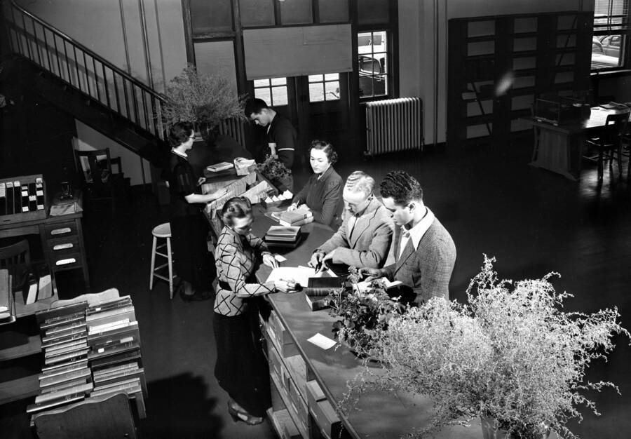 1950 photograph of the Library. Students get assistance from librarians at the loan desk. [PG1_201-31]