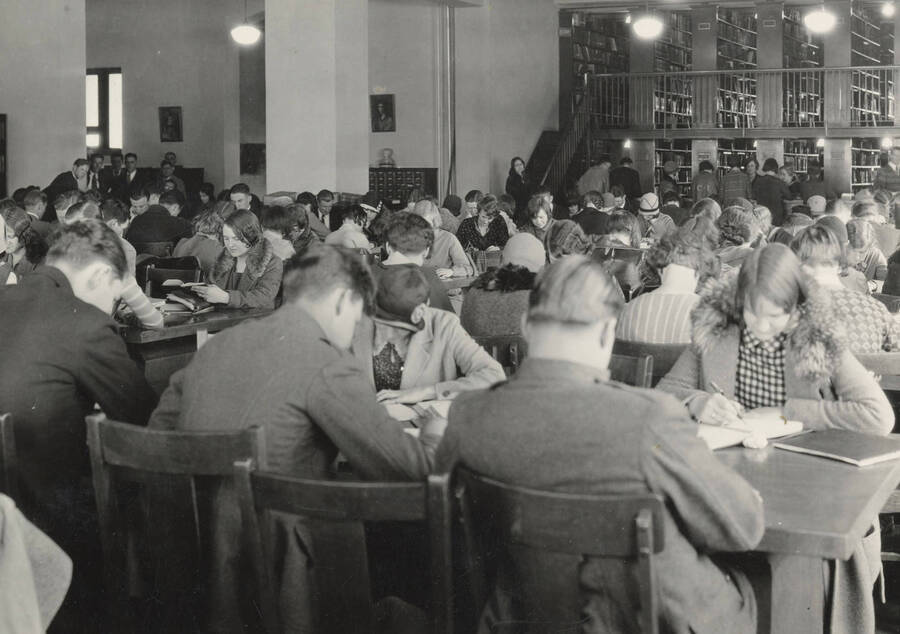 1930 photograph of the Library. Students studying with stacks in the background. [PG1_201-06]
