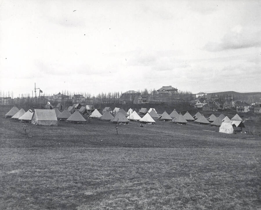 1910 photograph of Military Science Cadets. Tent encampment. University buildings in background. [PG1_208-001]