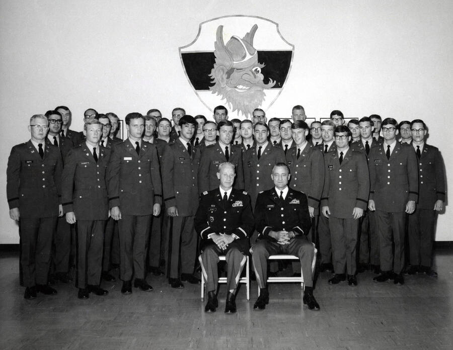 1969 photograph of Military Science Cadets. Newly commissioned officers in front of an image of Joe Vandal. Donor: Army ROTC. [PG1_208-116]