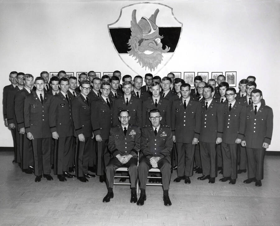 1968 photograph of Military Science Cadets. Newly commissioned officers in front of an image of Joe Vandal. Donor: Army ROTC. [PG1_208-118]