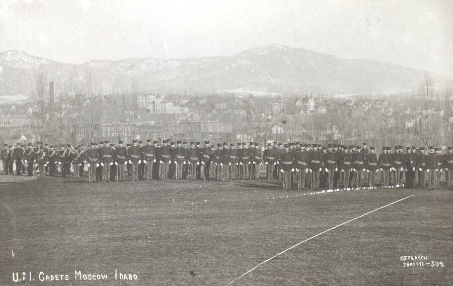 1919 photograph of Military Science Cadets. Military cadet battlion in formation oncampus. Campus buildings in the background. [PG1_208-023]
