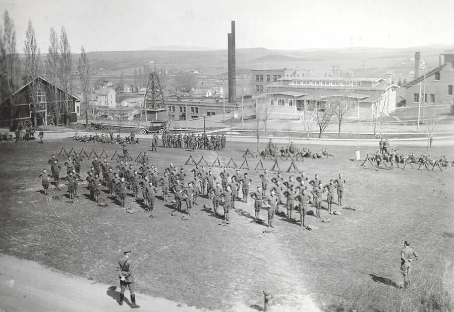 1922 photograph of Military Science Cadets. Military cadets participating in phycial exercise on campus. Campus buildings in the background. [PG1_208-025]