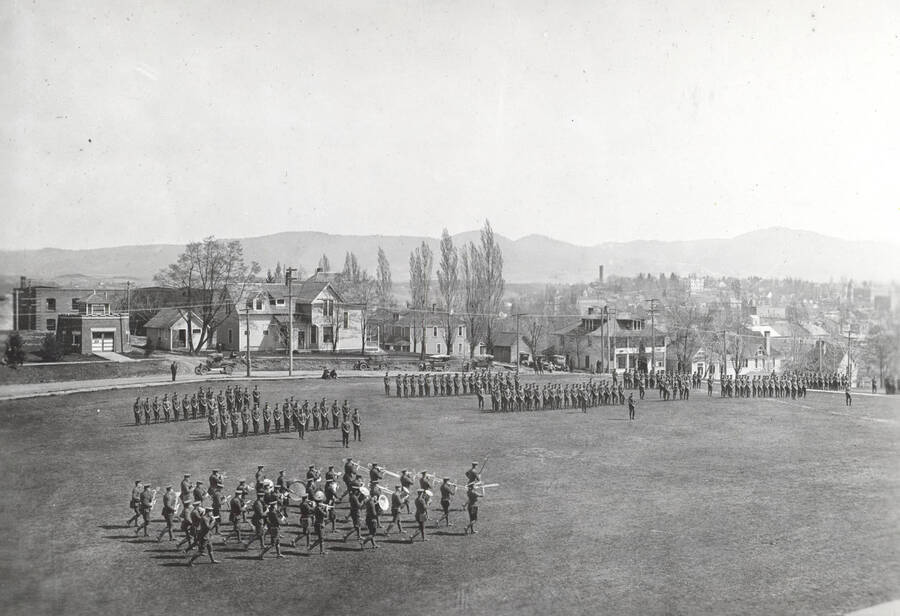 1922 photograph of Military Science Cadets. Military cadets on parade on campus grounds. Campus buildings in the background. [PG1_208-026]