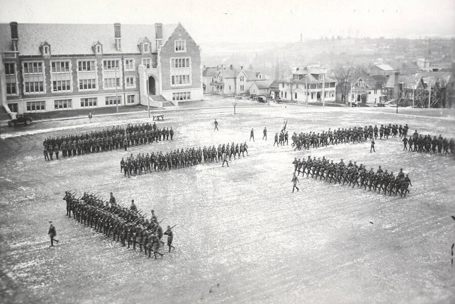 1925 photograph of Military Science Cadets. Military cadets on parade in front of the Sience Hall with campus buildings in the background. [PG1_208-034]