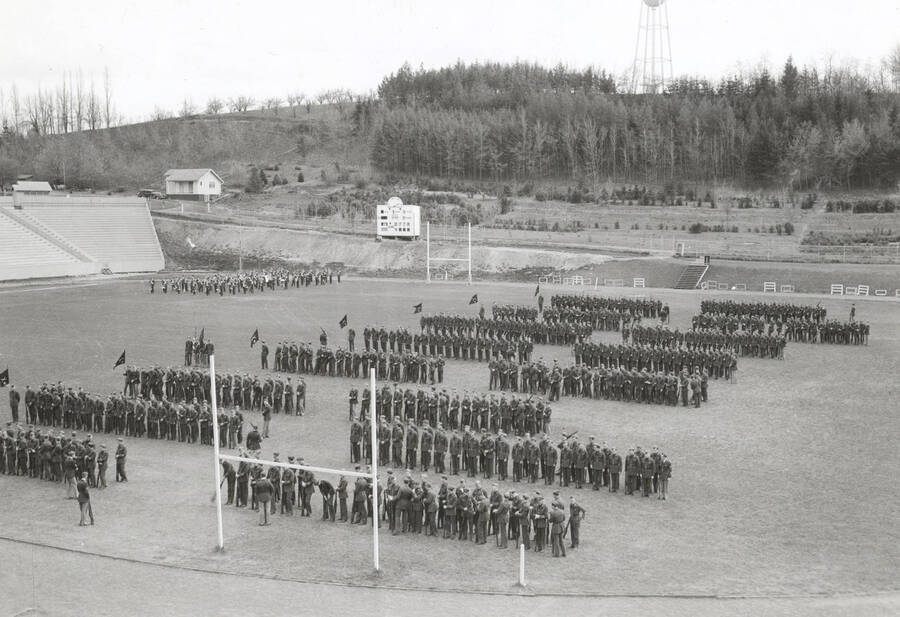 1935 photograph of Military Science Cadets. Military cadets on inspection at MacLean Field. 'I' Tower is visible on the hillside in the background. [PG1_208-041]