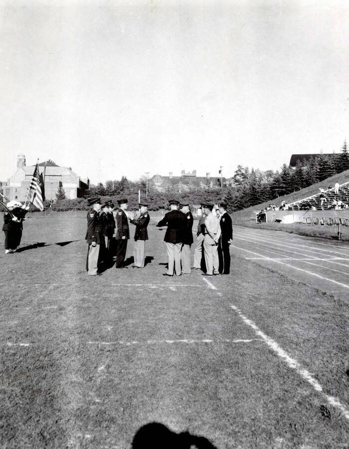 1953 photograph of Military Science Cadets. Cadet receiving an adward at MacLean Field. Campus buildings visible in the background. [PG1_208-076]