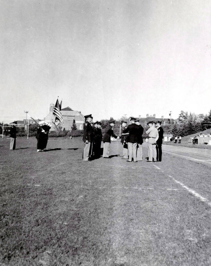 1953 photograph of Military Science Cadets. Cadet receiving an adward at MacLean Field. Campus buildings visible in the background. [PG1_208-077]