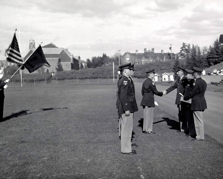 1953 photograph of Military Science Cadets. Cadet receiving an adward at MacLean Field. Campus buildings visible in the background. [PG1_208-078]