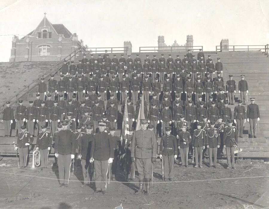 1915 photograph of Military Science Cadets. Battalion group in formation. University buildings visible in background. [PG1_208-009]