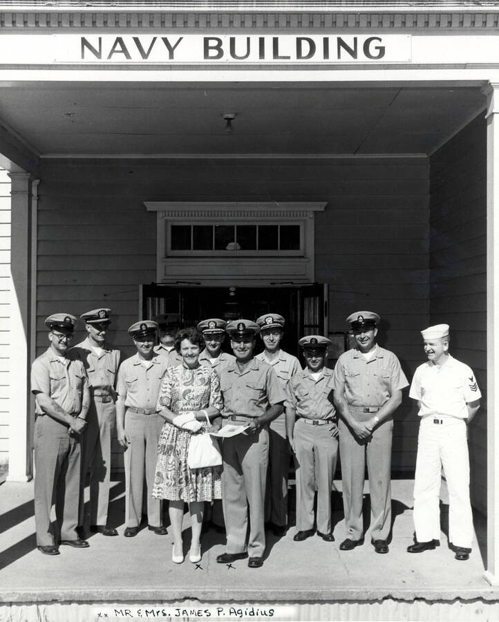 1962 photograph of Naval Science. Naval Science staffs stands in front of the Navy Building. Mr. And Mrs. James P. Agidius at front. Donor: Publications Dept.. [PG1_209-16]