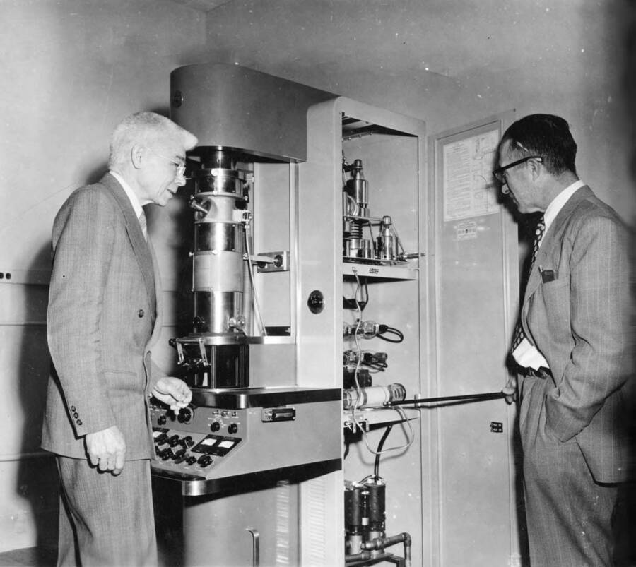 1957 photograph of Chemistry Class. Proffessor William H. Cone and an unidentified man examine an apparatus. negative buckling. [PG1_211-15]