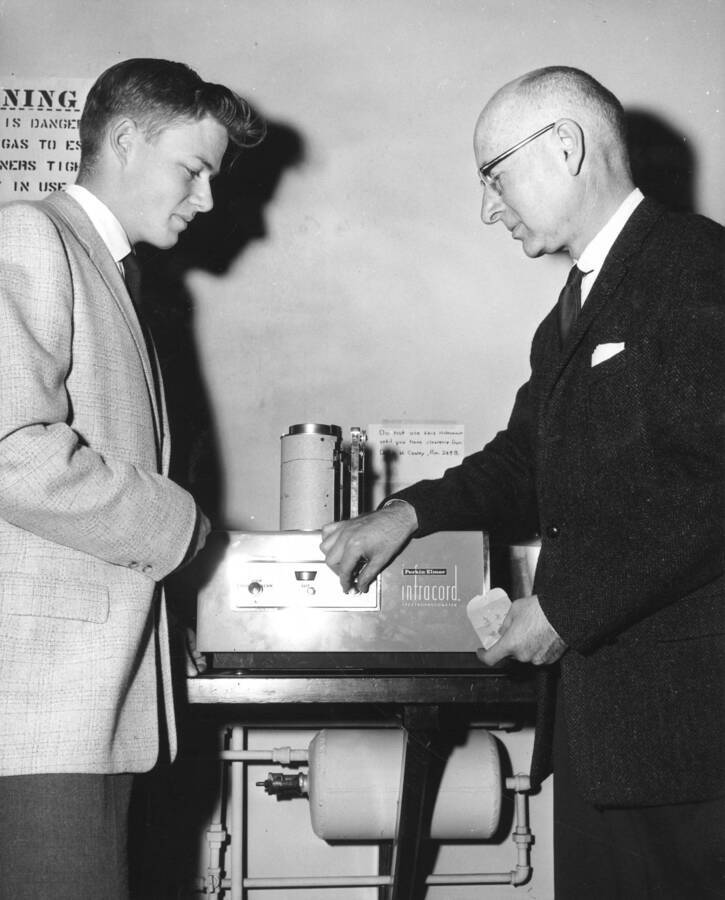 1961 photograph of Chemistry Class. Keith Watenpaugh and Malcom Renfrew examine a spectrophotometer. Donor: Publications Dept. [PG1_211-18]