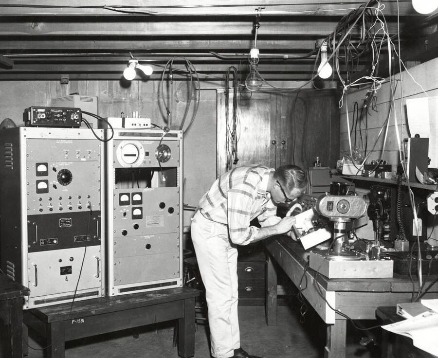 1961 photograph of Physics building. Student works with equipment in the lab. [PG1_213_02]