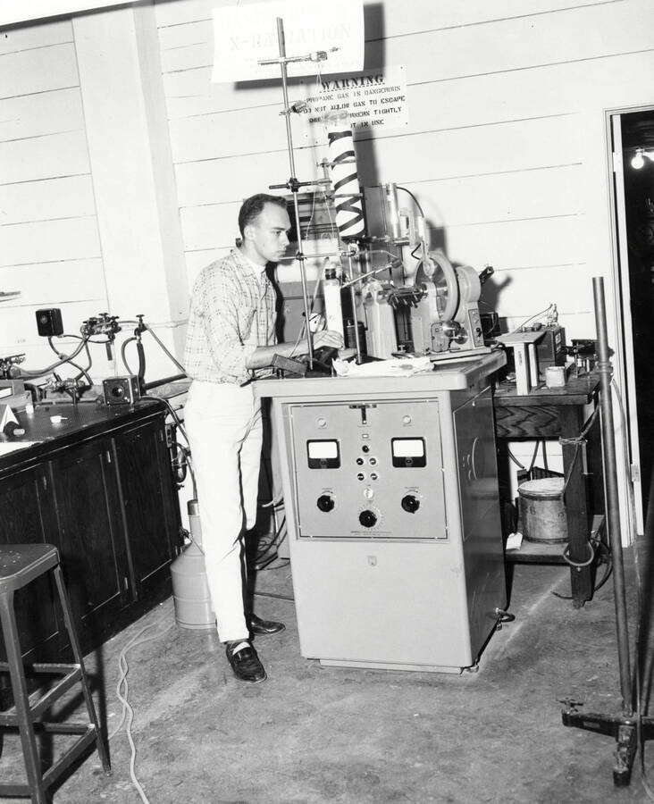 1961 photograph of Physics building. Student works with equipment in the lab. [PG1_213_03]