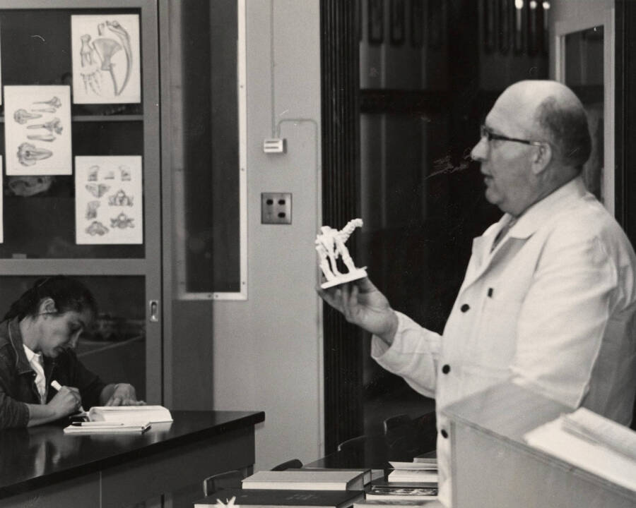 1965 photograph of Zoology building. Professor holds a small skeleton while giving a lecture. [PG1_214_27e]