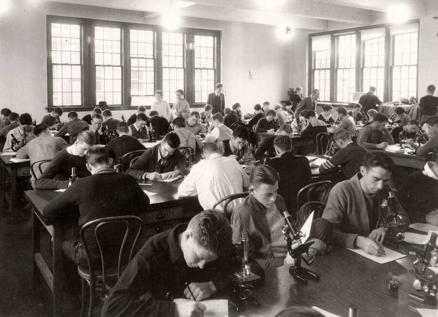 1938 photograph of Botany building. Students work with microscopes in the lab. [PG1_215_01]