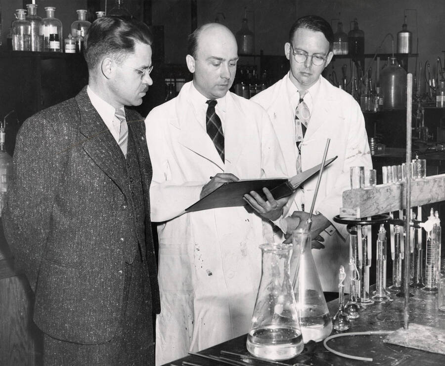 1948 photograph of Agricultural chemistry building. Faculty examines an experiment in the lab. [PG1_216_08]